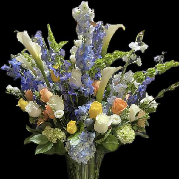 Tall mixed bouquet of blue and white flowers in a clear glass vase