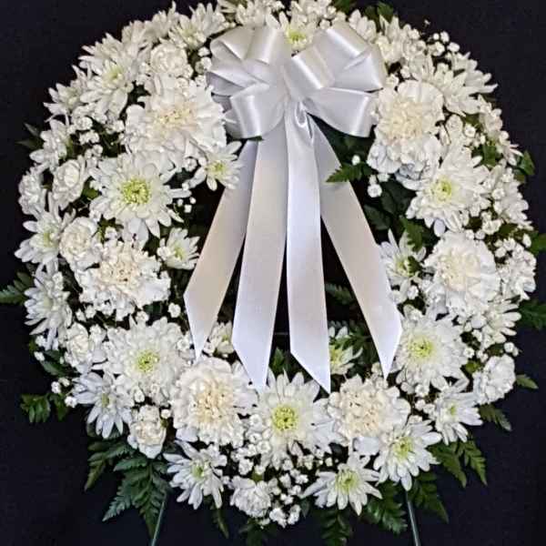 White floral funeral wreath with a satin bow on a dark background