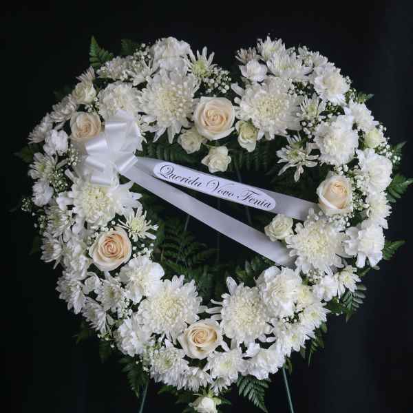 Heart-shaped white floral wreath on a stand with a ribbon bow