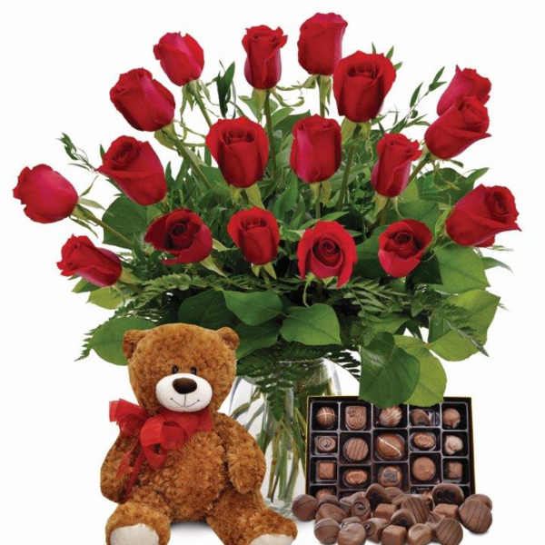 Red roses in a glass vase with a teddy bear and box of chocolates