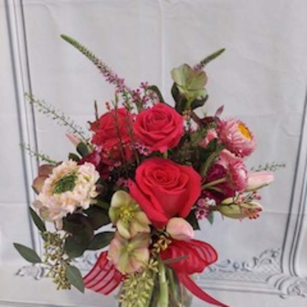 Bouquet of red roses and mixed pink flowers in a glass vase with a red ribbon