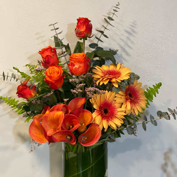 Orange roses, calla lilies, and yellow gerbera daisies in a glass vase