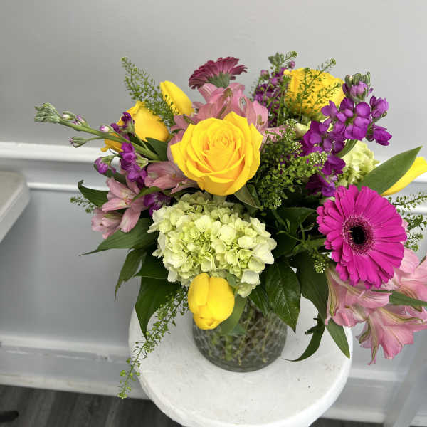 Mixed arrangement of yellow roses and tulips with pink and purple blooms in a clear glass vase