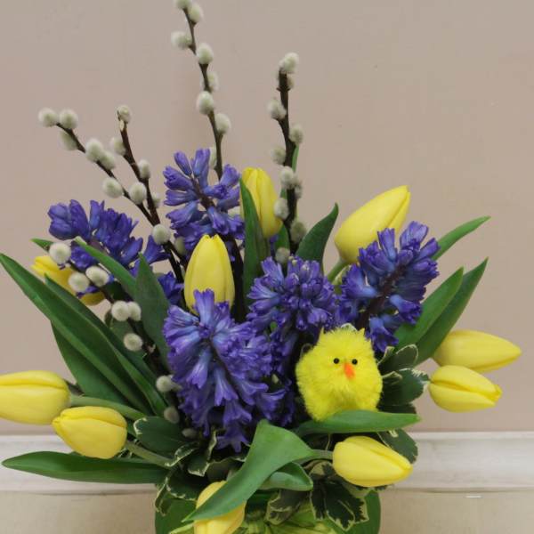 Spring arrangement of yellow tulips and blue hyacinths with pussy willow branches and a small yellow chick decoration