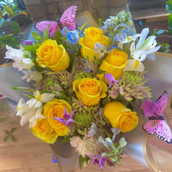 Bouquet of yellow roses with white and purple flowers and pink butterfly picks