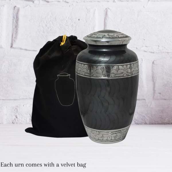 Black memorial urn with silver detailing beside a velvet bag