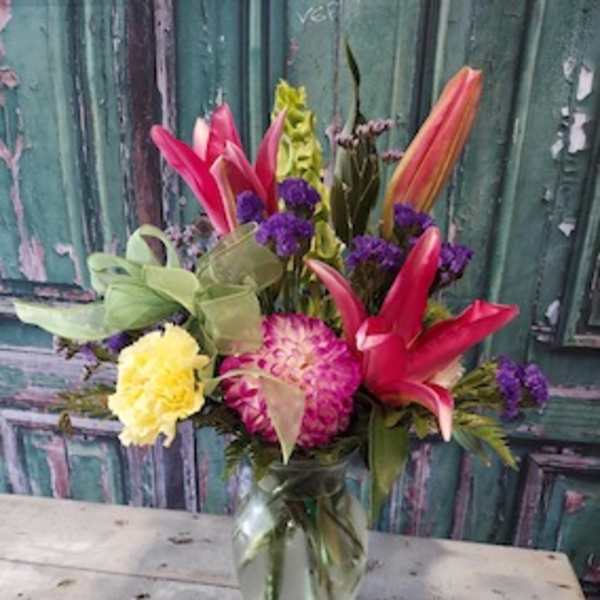Mixed bouquet with pink lilies, yellow carnations, and purple flowers in a glass vase