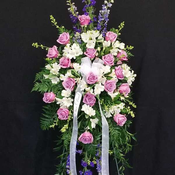 Standing floral spray with pink roses, white blooms, and purple accents on a black background