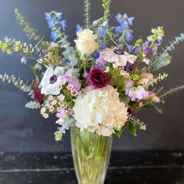 Mixed bouquet in a clear glass vase with white, blue, and pink flowers