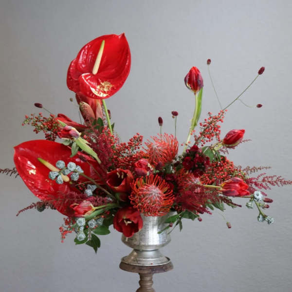 Red floral arrangement in a silver pedestal vase with tall tropical blooms