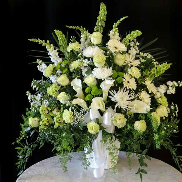 White and pale green floral arrangement in a white vase with ribbon