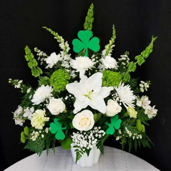 White floral arrangement with lilies, roses, and green shamrock picks in a white vase