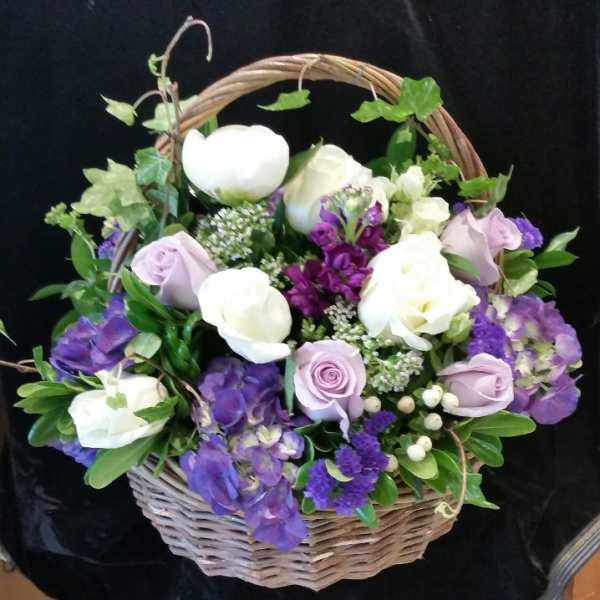 Basket arrangement of white and lavender roses with purple flowers