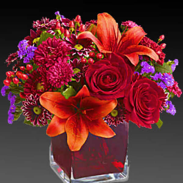 Red and orange floral arrangement in a clear square vase