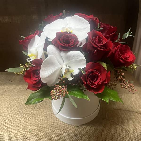 Red roses and white orchids arranged in a white hatbox