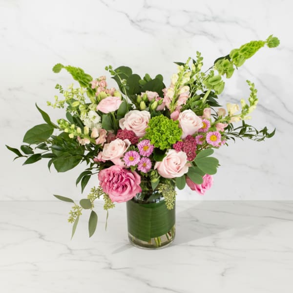 Arrangement of pink roses and mixed blooms with green hydrangea in a clear glass vase