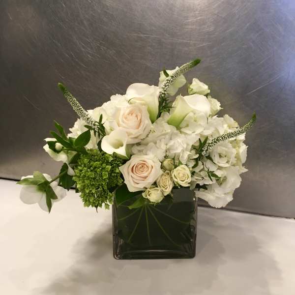 White floral arrangement in a square glass vase with roses and hydrangeas