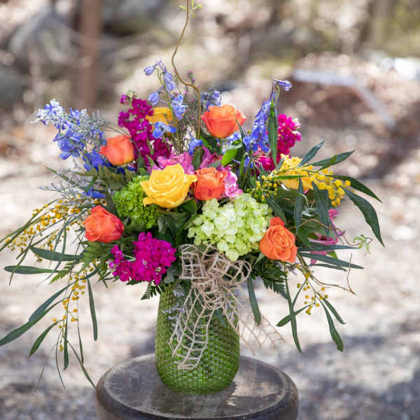 Colorful bouquet of roses, blue flowers, and hydrangea in a green vase