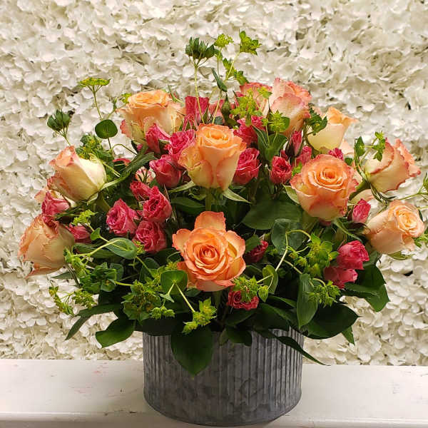 Round arrangement of peach roses and pink spray roses in a gray metal cylinder vase