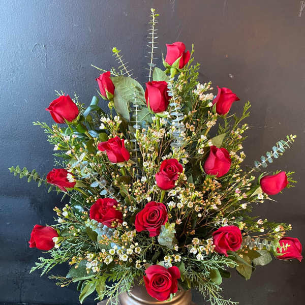 Red roses arranged in a gold vase with mixed greenery
