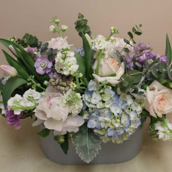 Pastel floral arrangement in a gray container with roses and hydrangeas