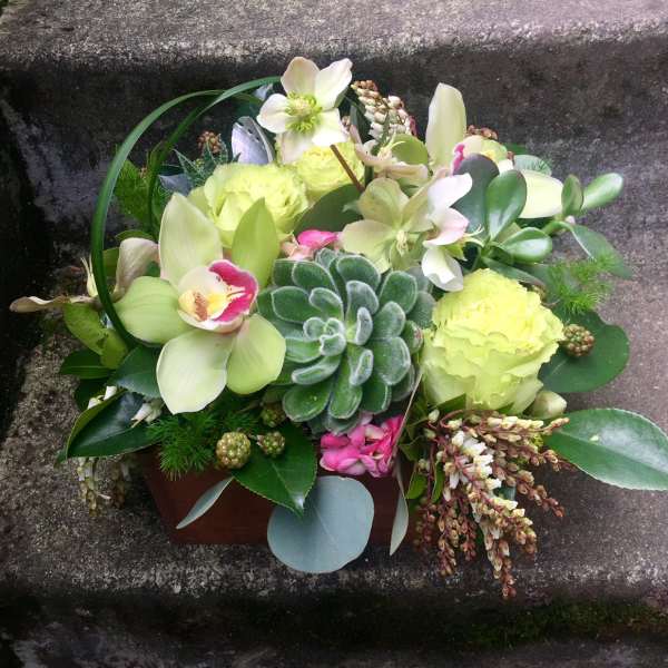 Compact floral arrangement with pale green blooms and succulents in a low container