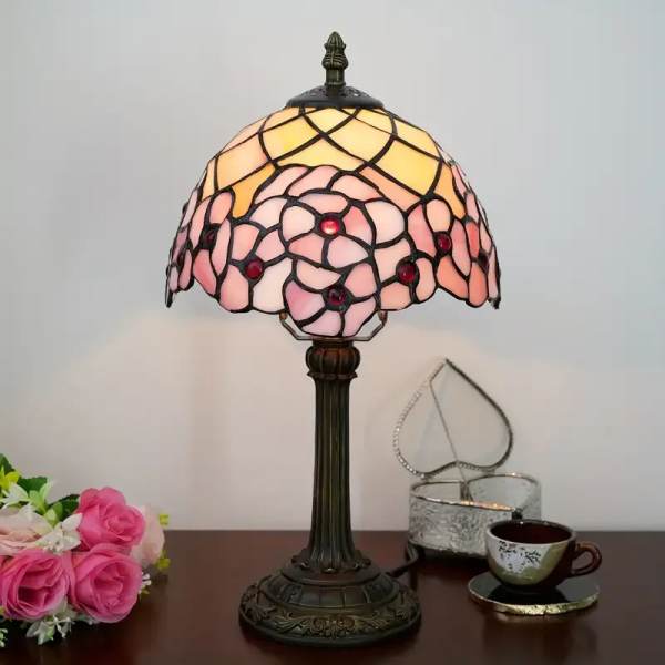 Stained-glass table lamp with pink and yellow shade beside a small rose bouquet