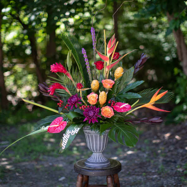 Tropical floral arrangement in a gray urn vase with bright pink and orange blooms