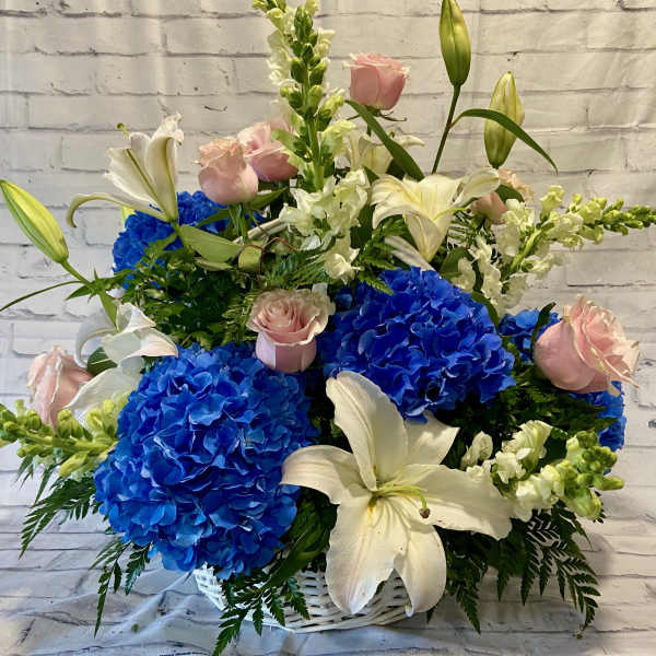Blue hydrangeas and white lilies with pink roses in a white basket