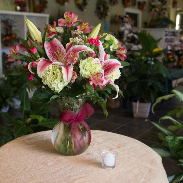 Pink lilies and hydrangeas arranged in a glass vase with a ribbon