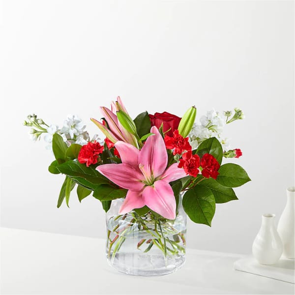 Pink lilies, red carnations, and white flowers in a clear glass vase