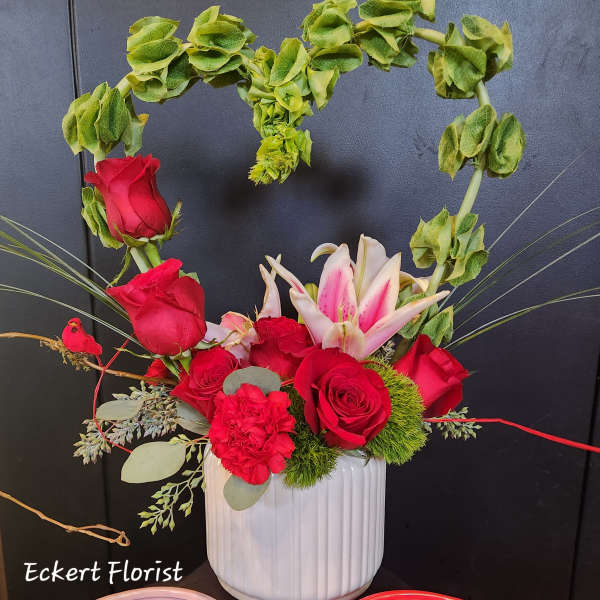 Red roses and pink lilies in a white vase with a heart-shaped greenery arch