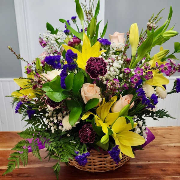 Basket arrangement with yellow lilies, pale roses, and purple flowers