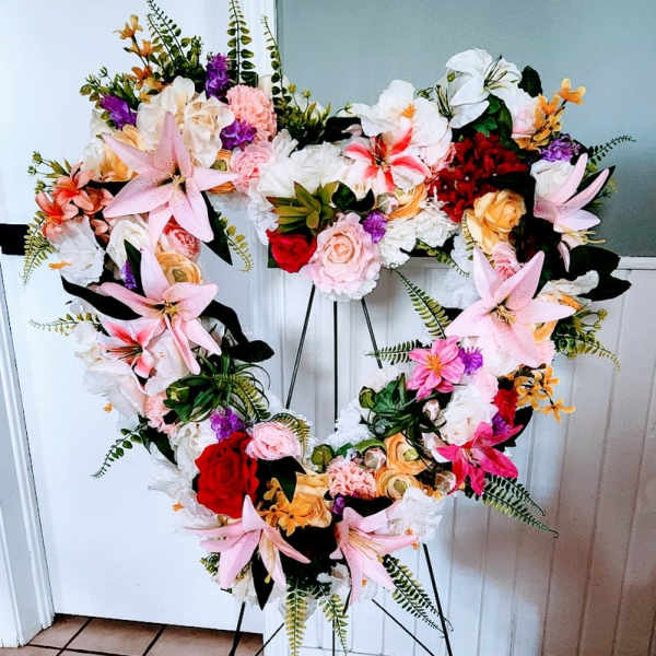 Heart-shaped floral wreath on a stand with pink, white, red, and orange flowers