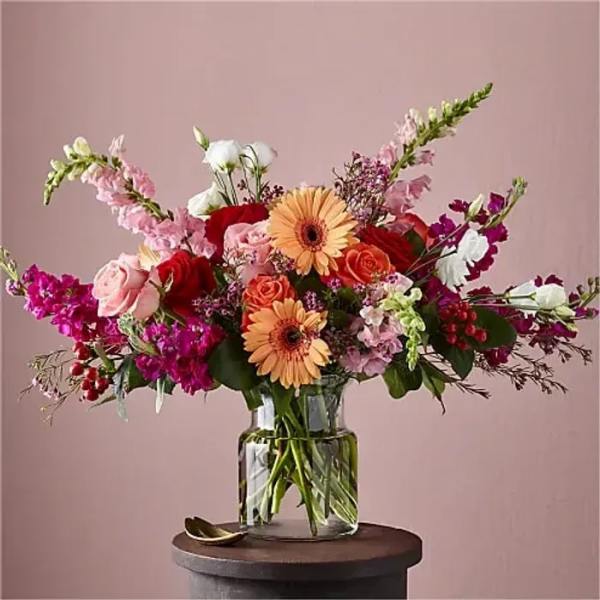Mixed bouquet of pink, red, white, and peach flowers in a clear glass vase