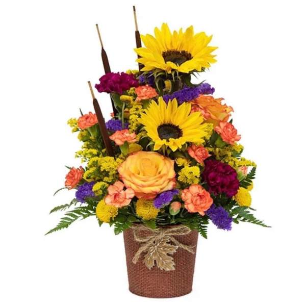 Tiered floral arrangement with sunflowers, roses, and carnations in a burlap-wrapped pot