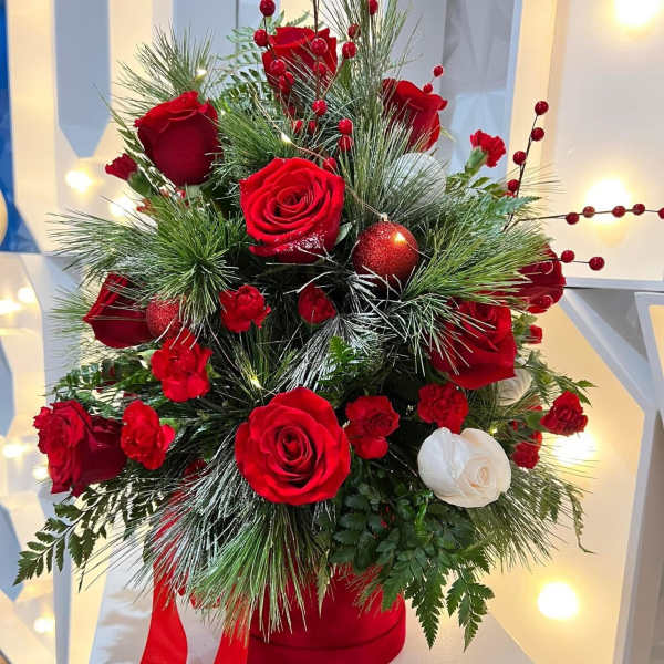 Red and white roses arranged with pine and berries in a red hatbox