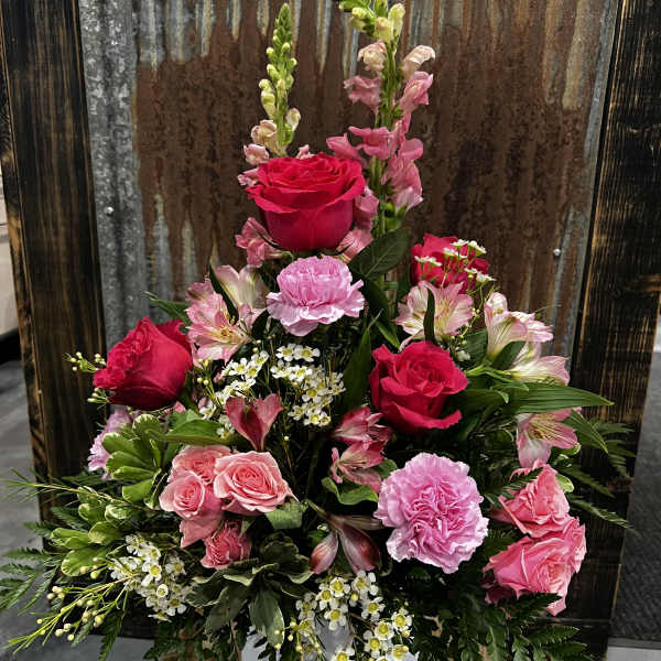 Pink and red roses arranged in a white vase with mixed filler flowers.