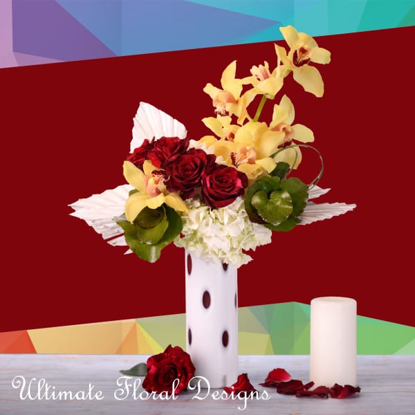 Red roses and yellow orchids in a white vase with a candle beside it