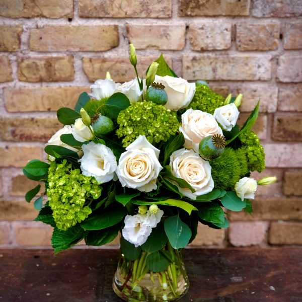 White roses and green blooms arranged in a glass vase