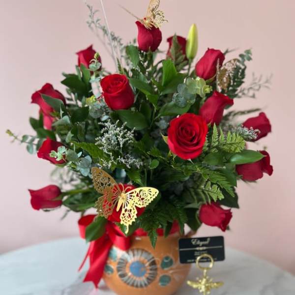 Red roses arranged in a decorated vase with a ribbon and butterfly pick