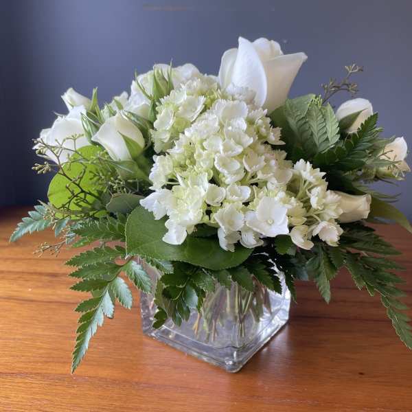 Low arrangement of white roses and hydrangeas in a clear glass cube vase
