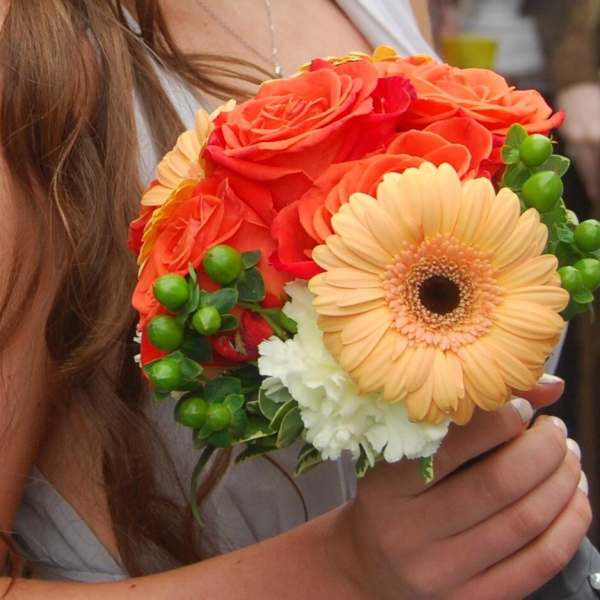 Handheld bouquet of orange roses, a peach gerbera daisy, and white carnations