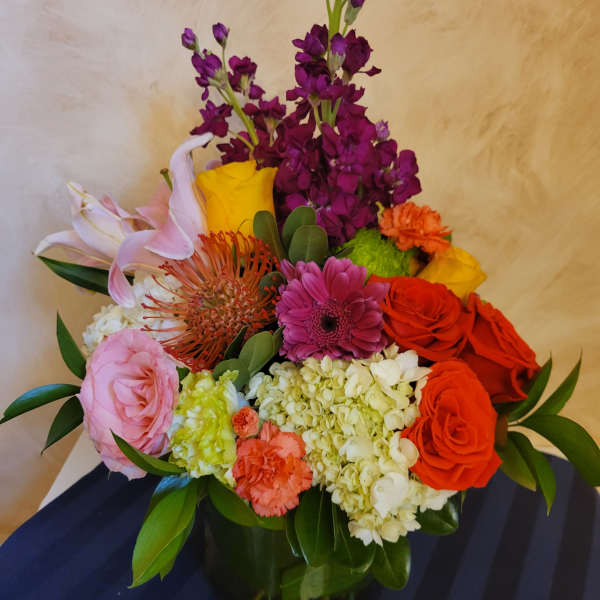 Mixed bouquet in a dark vase with roses, lilies, hydrangea, and bright accent flowers