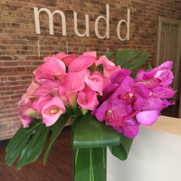 Pink calla lilies and purple orchids in a tall glass vase