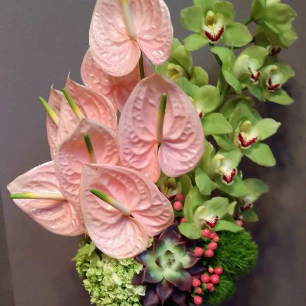 Pink anthuriums and green orchids in a tall blue vase