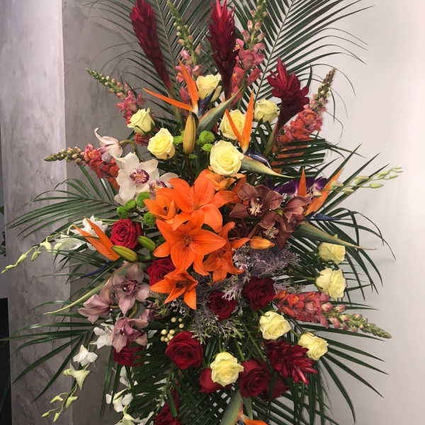 Tall tropical floral spray with orange lilies, roses, and orchids