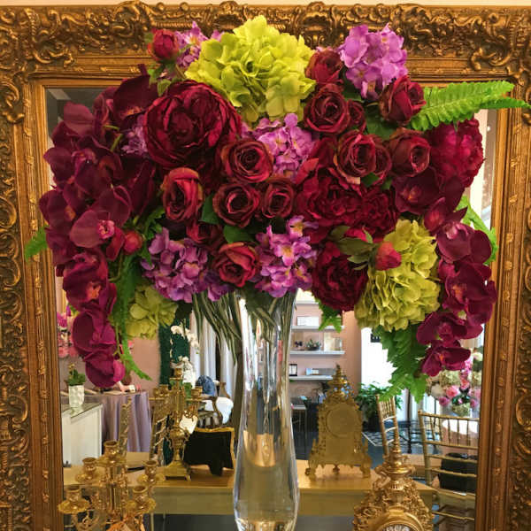 Large floral arrangement in a clear glass vase with burgundy, purple, and lime blooms