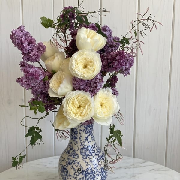 White roses and purple lilacs in a blue-and-white vase