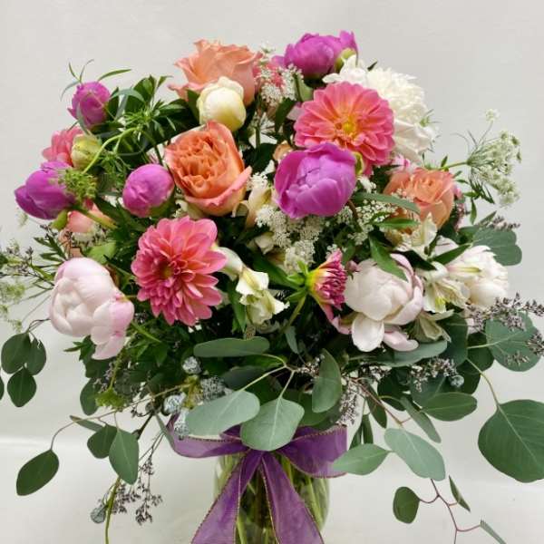 Mixed pink and peach bouquet in a glass vase with a purple ribbon